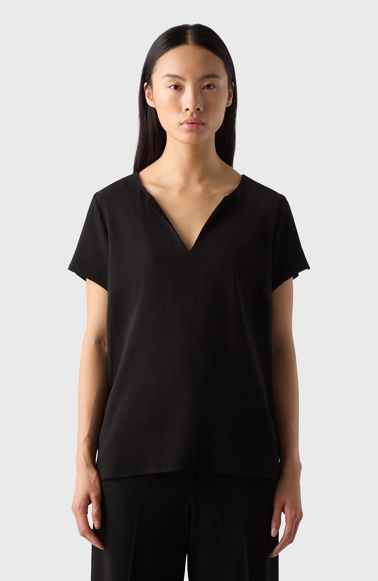 A woman wearing a black V-neck top with short sleeves, made of soft crèpe fabric, paired with black pants.
