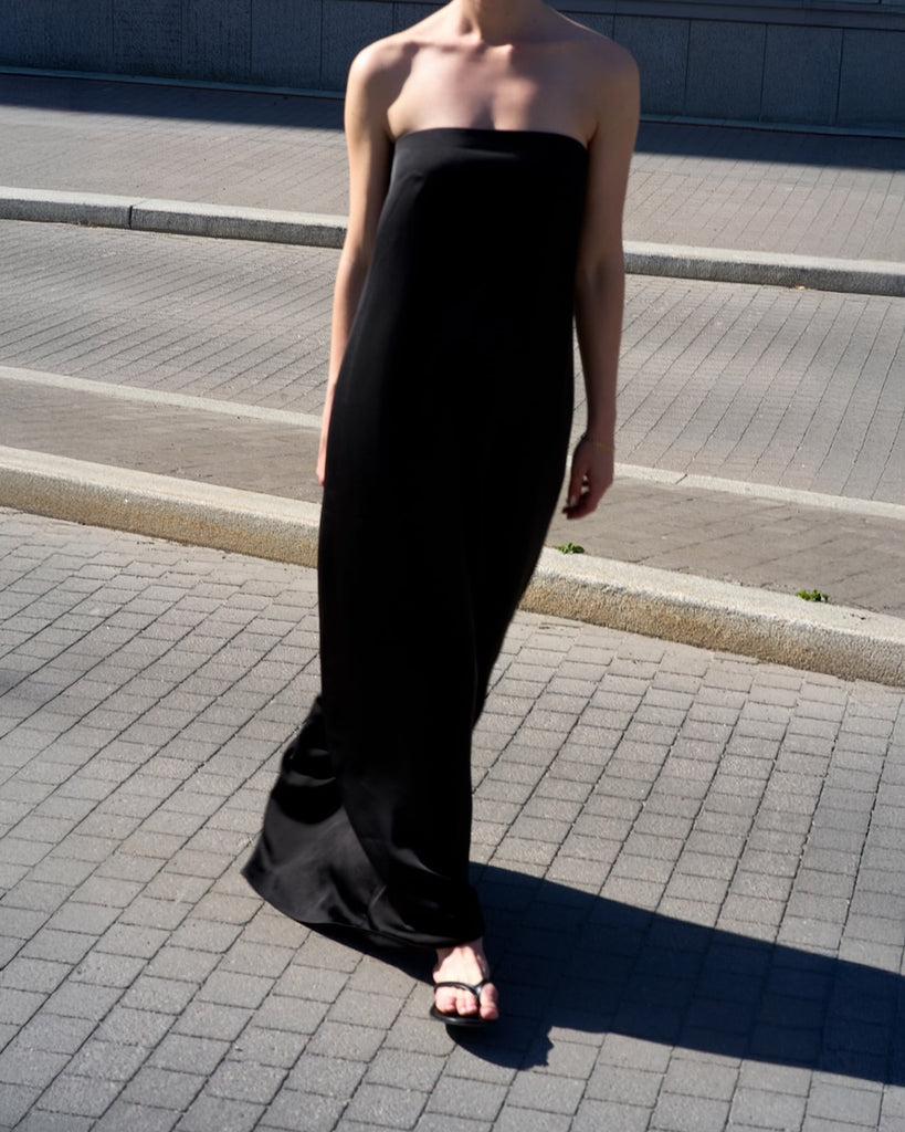 Person wearing a black strapless dress standing on a sidewalk.