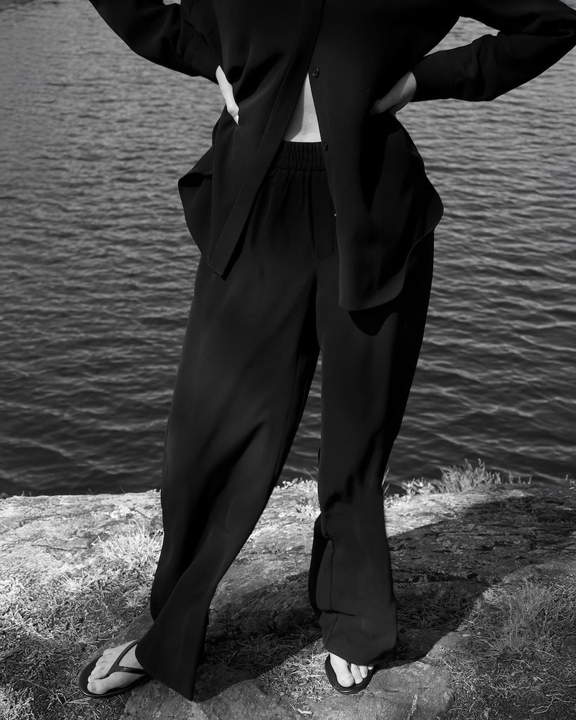 Person wearing a black suit standing by a body of water